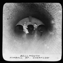 A historic picture of two women sitting in a brand new drainage pipe, circa 1898
